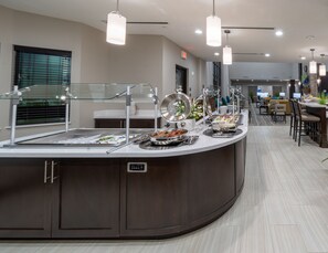 A buffet area with a variety of food options, a seating area with tables and chairs, and a modern design with pendant lighting.