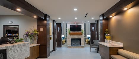 A hotel lobby with a reception desk, seating area, fireplace, and a TV mounted on the wall.