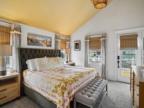 A bedroom with a large bed, a bench, a dresser, and a view of a building through the window. - Coastal Home w/ Private Hot Tub, Block to Beach (Bethany Beach)