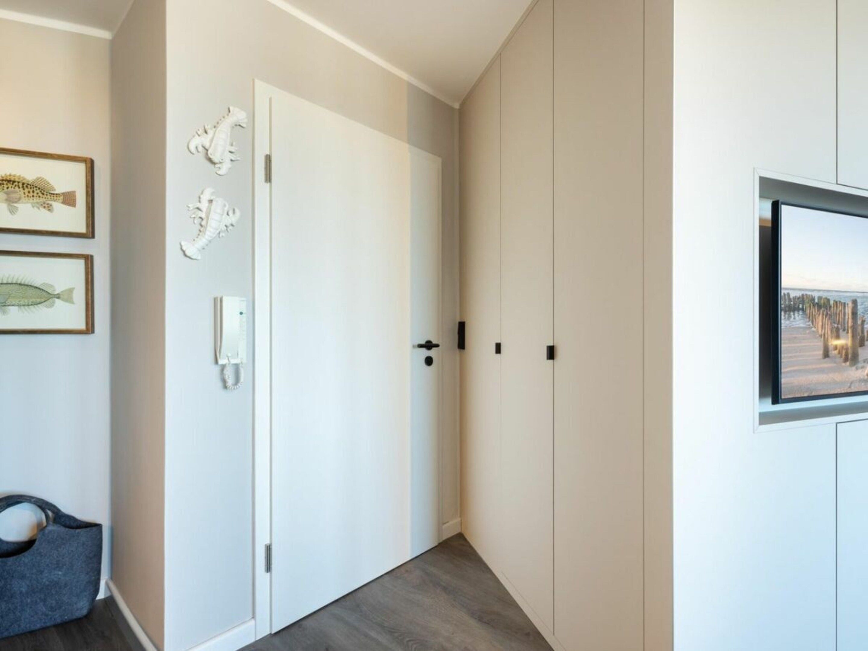 A hallway with a white door, a coat rack, and a framed picture of fish on the wall.