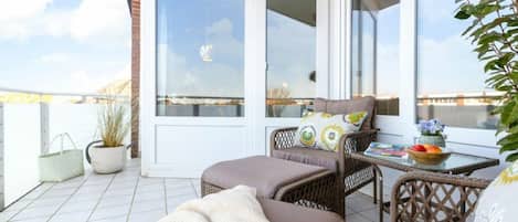 A balcony with wicker furniture, a table with a bowl of fruit, and a potted plant.