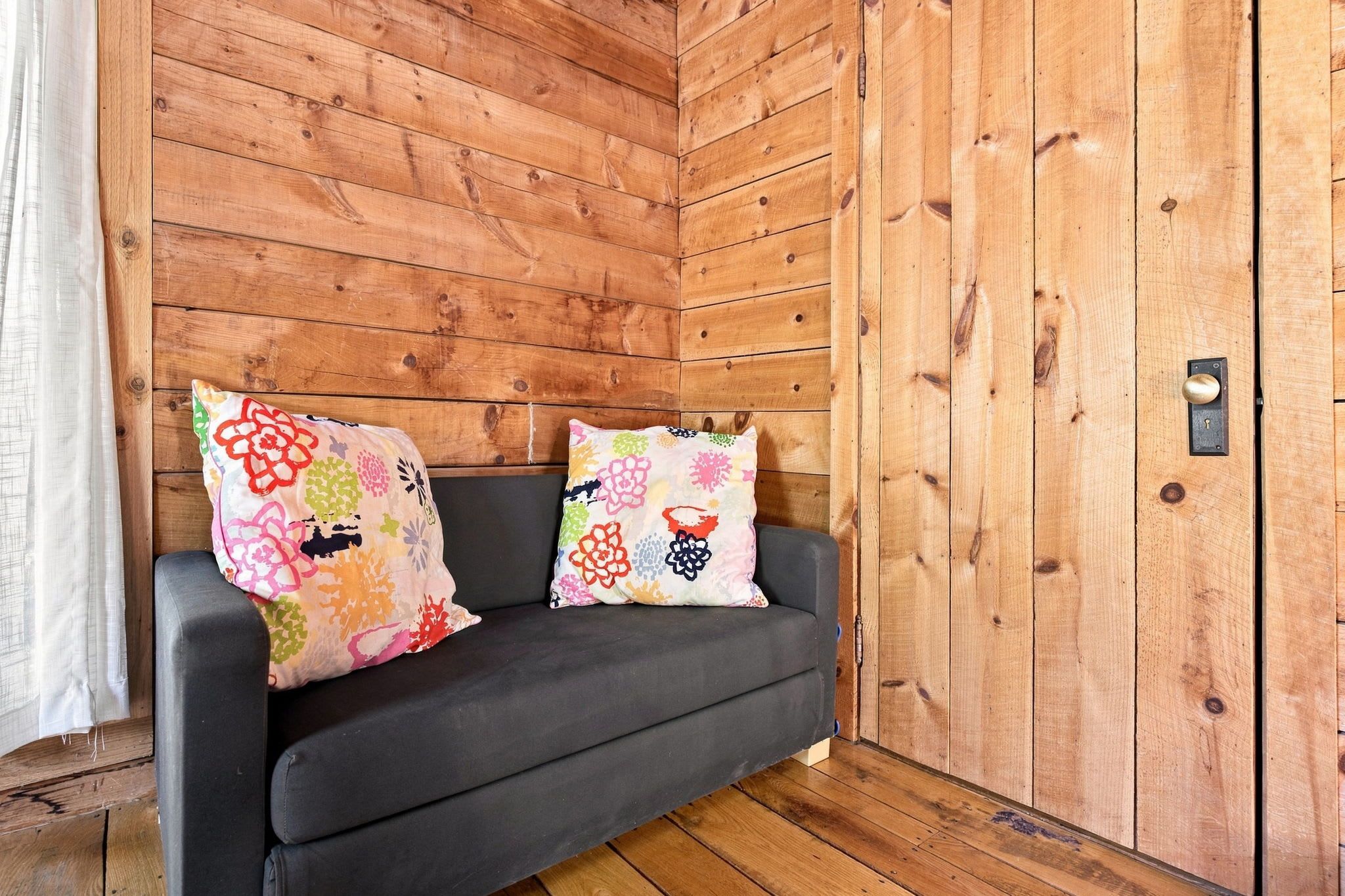A wooden cabin interior with a dark grey sofa and colorful floral cushions.