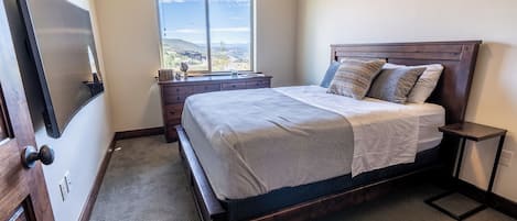 Un dormitorio con cama, cómoda, mesita de noche, ventana con vistas y puerta.