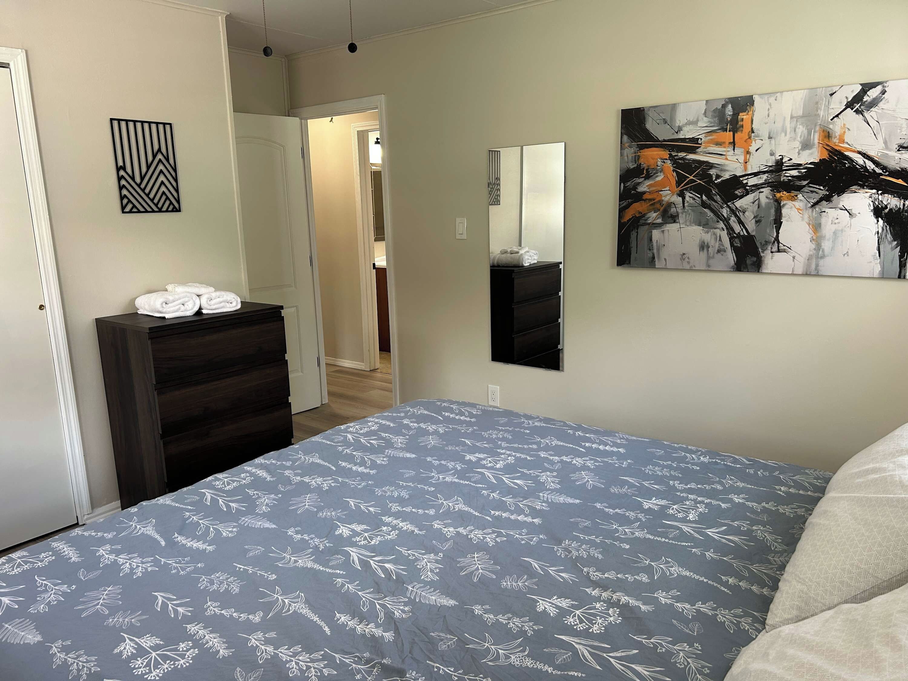 A bedroom with a bed, a dresser, a mirror, and artwork on the walls.