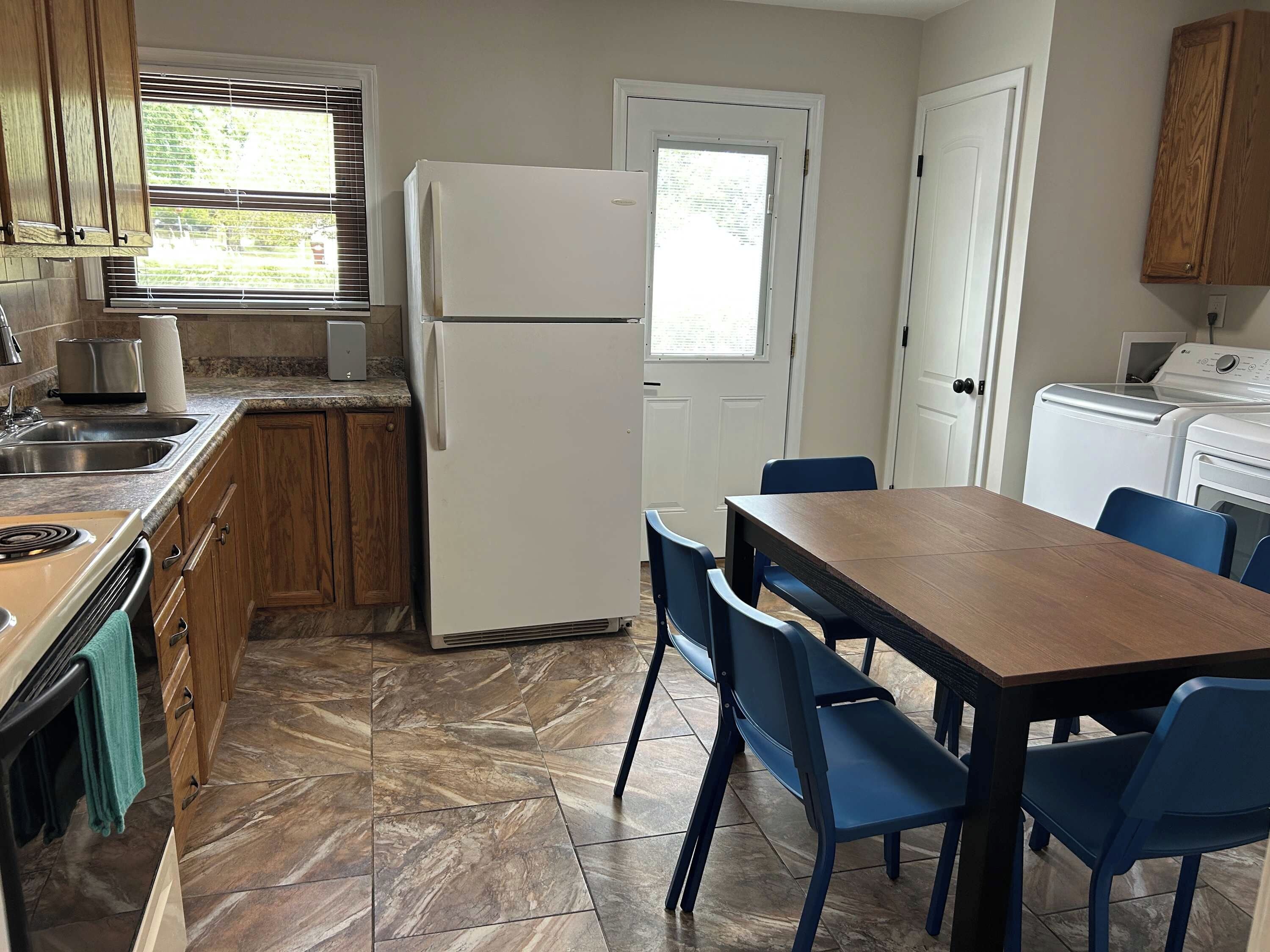 A compact kitchen with a refrigerator, stove, sink, and a dining area with chairs.