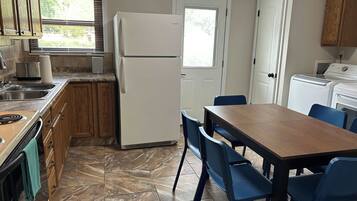 A compact kitchen with a refrigerator, stove, sink, and a dining area with chairs.