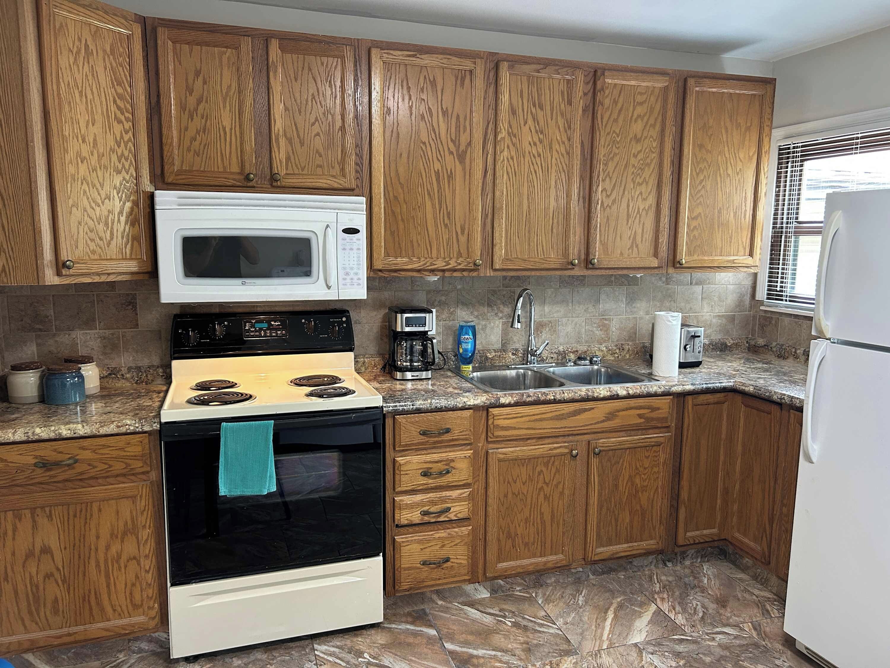 Una cocina con armarios de madera, un microondas blanco, una estufa, un fregadero y un refrigerador.