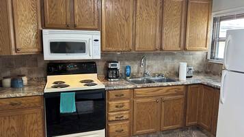 Una cocina con armarios de madera, un microondas blanco, una estufa, un fregadero y un refrigerador.