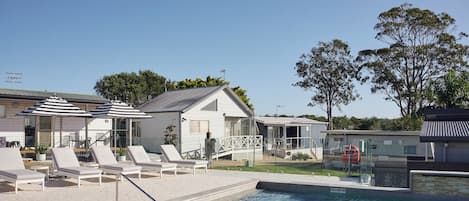 A swimming pool with lounge chairs, a small house, and a clear sky.