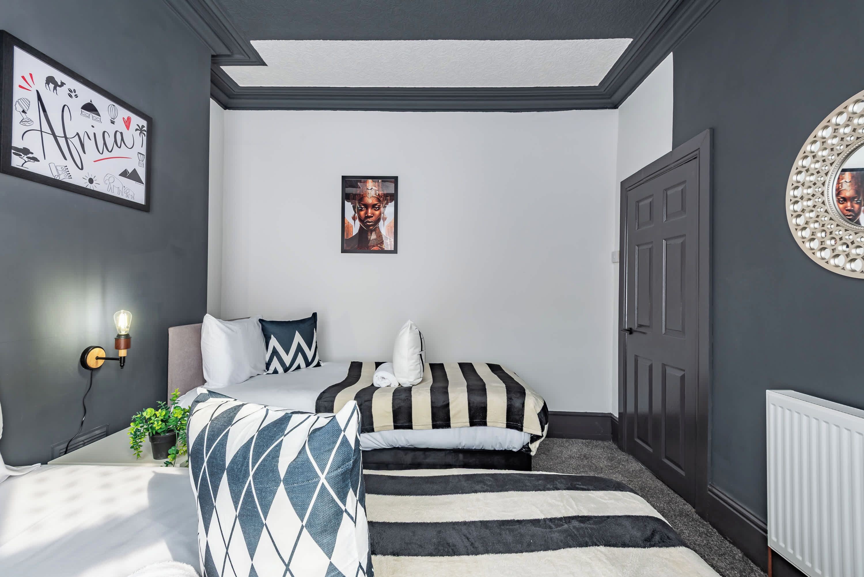 A bedroom with two beds, a wall-mounted light, a framed picture, and a door with a decorative mirror.