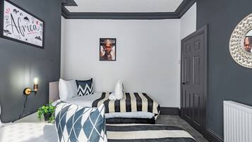 A bedroom with two beds, a wall-mounted light, a framed picture, and a door with a decorative mirror.