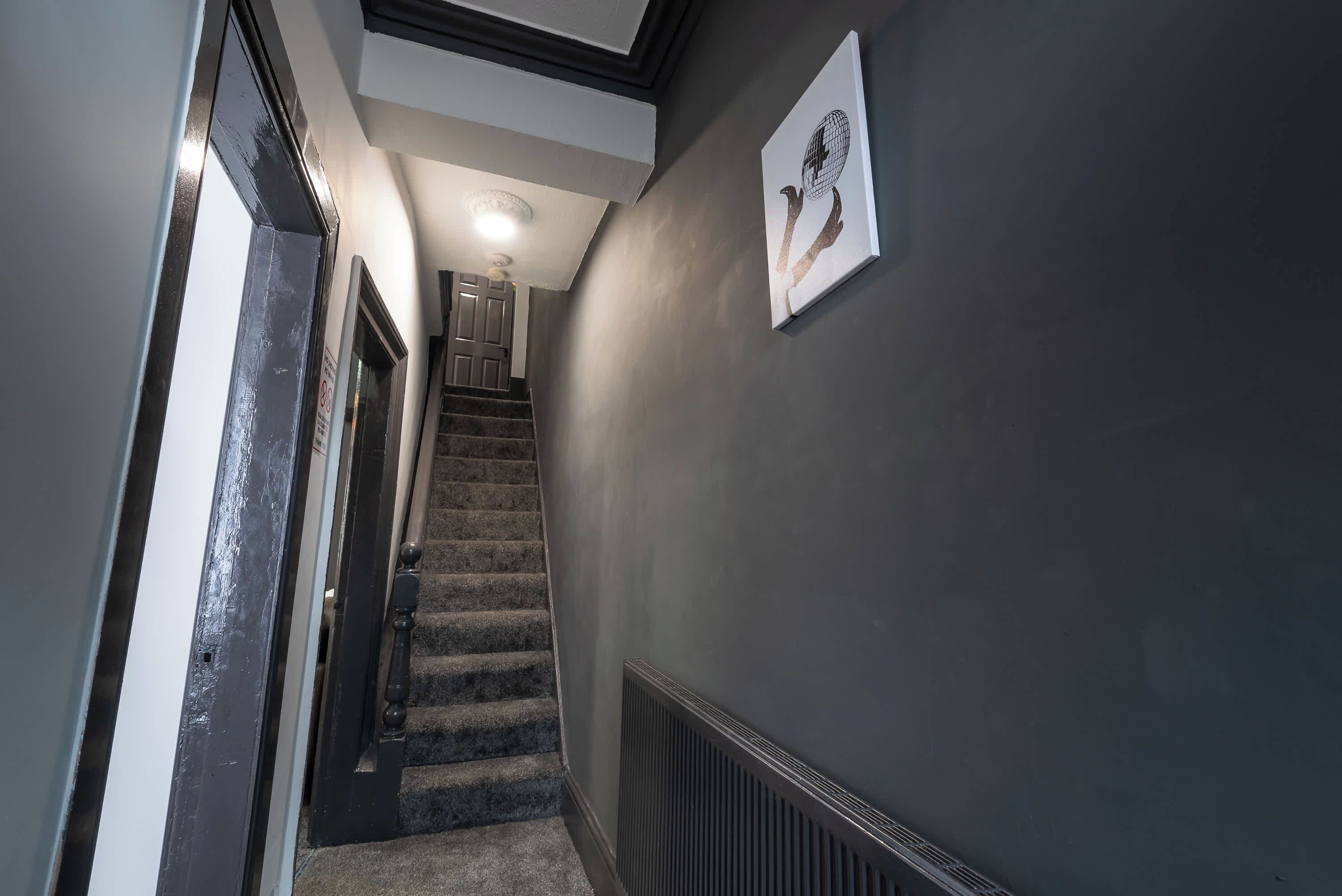 A hallway with a staircase leading to another room, a radiator on the wall, and a ceiling light.