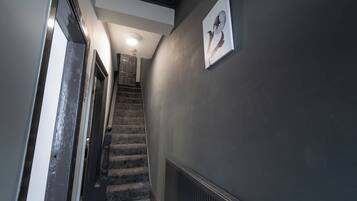 A hallway with a staircase leading to another room, a radiator on the wall, and a ceiling light.