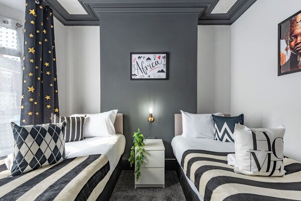 A modern bedroom with two beds, star-patterned curtains, a wall-mounted artwork, and a small bedside table with a plant. - Comfy 4 Bed House  2 Bathrms Great HU5 Shops Cafes (Kingston upon Hull)
