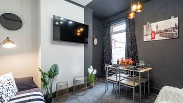 Un salon moderne doté d’un téléviseur à écran plat, d’un coin repas avec une table et des chaises, et offrant une vue sur l’extérieur grâce à une fenêtre.
