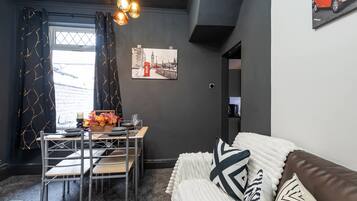 A modern living space with a dining area, a sofa, and a painting of a cityscape.