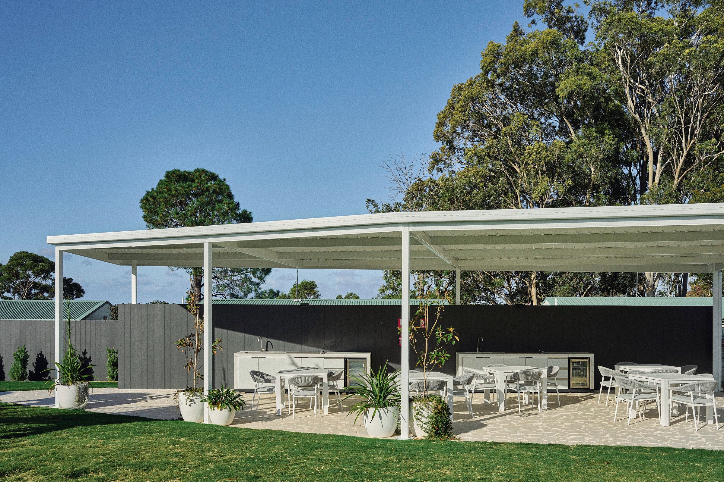 A covered outdoor patio with multiple tables and chairs, a grill, and potted plants.