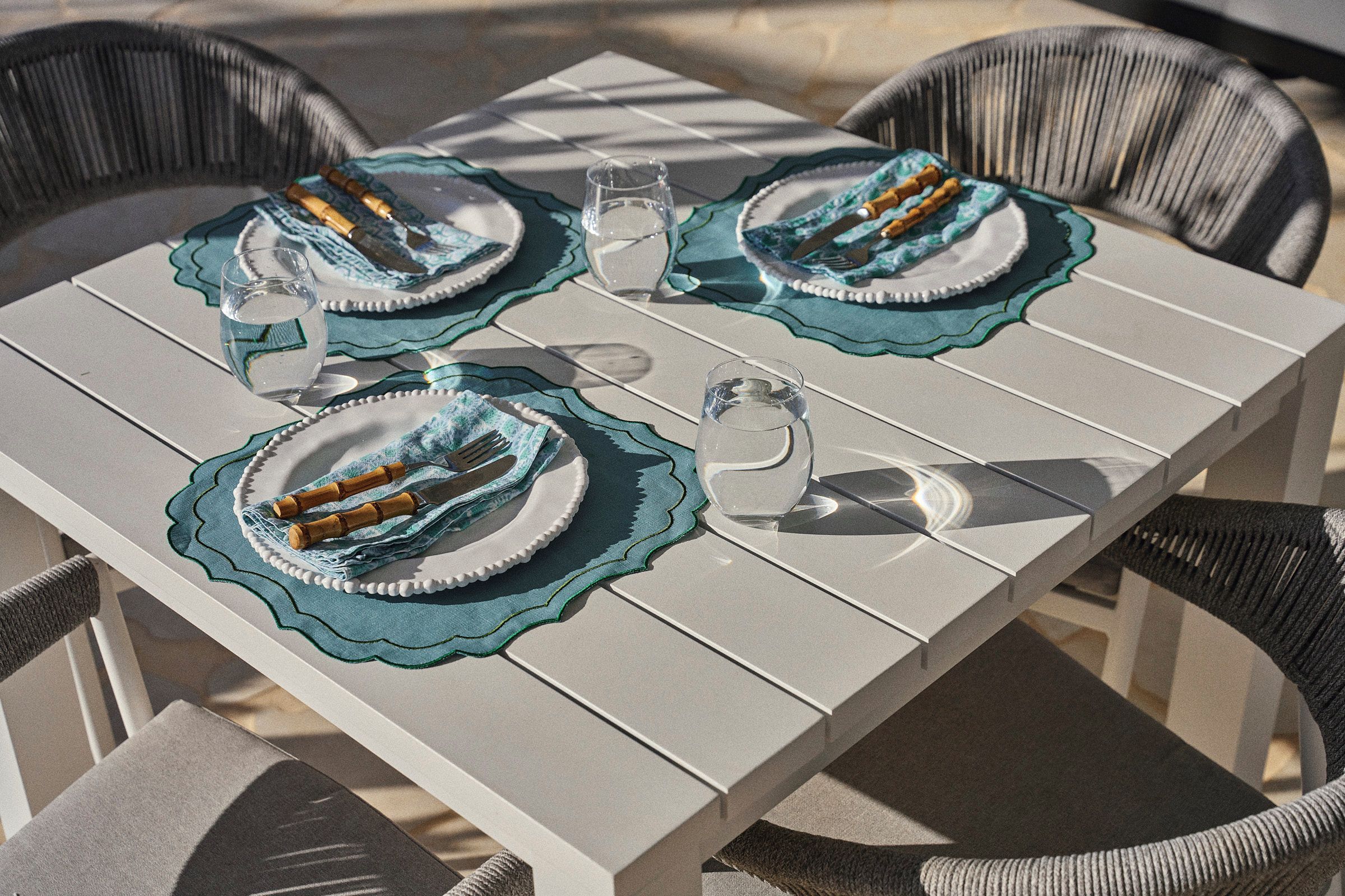 A table set with plates, cutlery, and glasses, surrounded by wicker chairs.