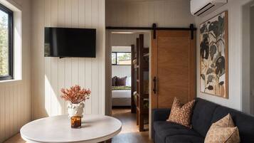 A room with a white round table, a dark sofa, a mounted TV, and a sliding door leading to another room.