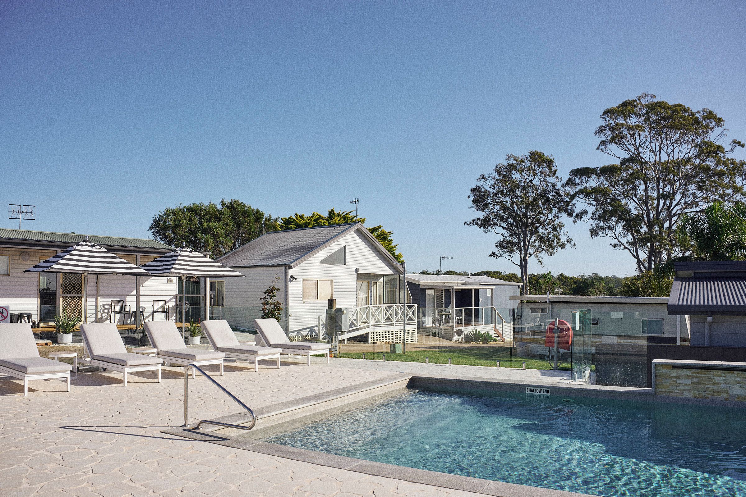 A swimming pool with lounge chairs, a small house, and a clear sky.