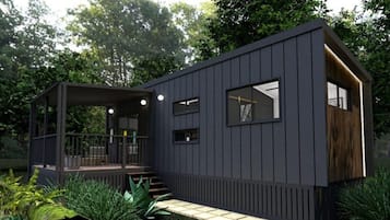 Una cabaña moderna de color oscuro con un porche cubierto, una pequeña terraza y un acceso pavimentado.