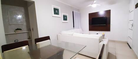 Una sala de estar moderna con una mesa de comedor de vidrio, un sofá blanco y un televisor de pantalla plana montado en la pared.