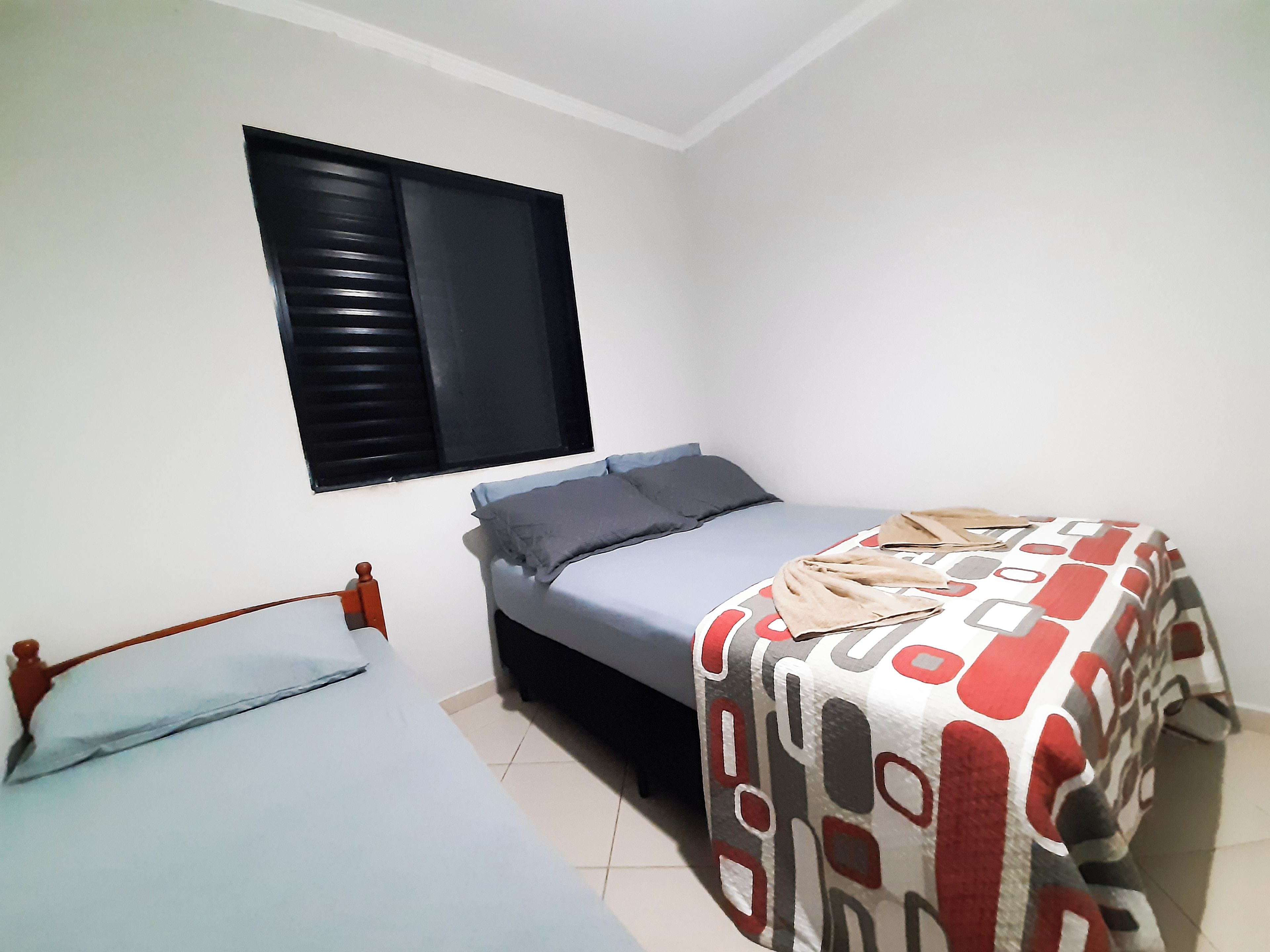 Ein Schlafzimmer mit einem Bett, einem Fenster mit Jalousien und einer gemusterten Bettdecke.
