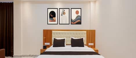 A hotel room with a large bed, a wooden headboard, a marble floor, and three framed artworks on the wall.