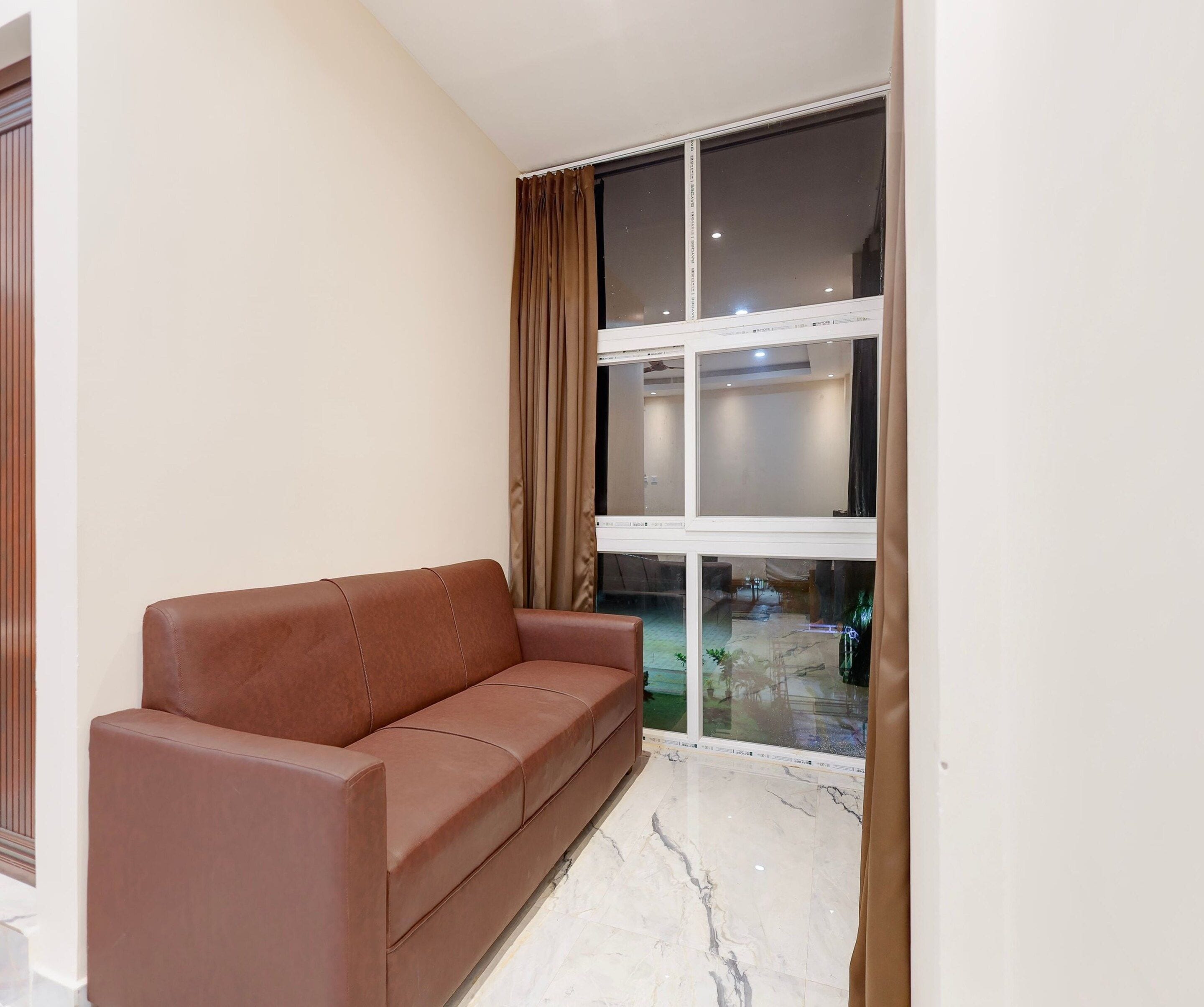 Ein Zimmer mit einem braunen Ledersofa, einem großen Fenster mit Vorhängen und einem Marmorboden.