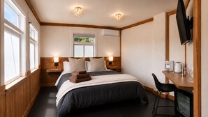 Una habitació d'hotel amb un llit, taules de nit, un televisor, un escriptori amb una cadira i una finestra.