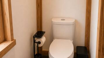 A small, compact bathroom with a white toilet, a black trash bin, and a toilet paper holder.