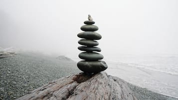Pilhas de pedras lisas equilibradas sobre uma superfície de madeira desgastada, com uma praia e oceano desfocados ao fundo.