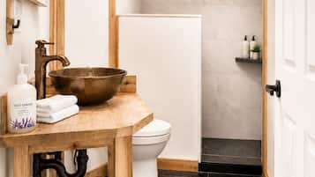 A bathroom with a wooden vanity, a large basin, a toilet, and a shower.