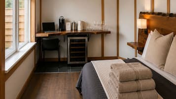 A bedroom with a bed, a desk with a laptop, a coffee maker, and a wine glass set.
