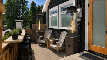 An outdoor seating area with wooden chairs and tables, a fire feature, and a signboard.
