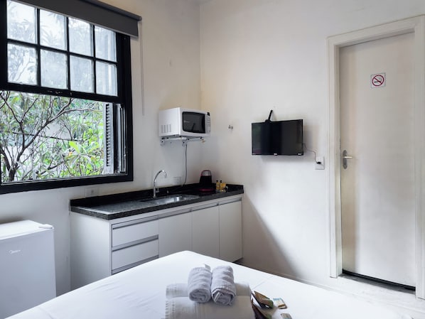 Habitación de hotel con cama, lavamanos, microondas, televisión y ventana con vistas a zonas verdes.