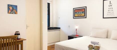 A bedroom with a bed, bedside table, lamp, and a wall with framed pictures.
