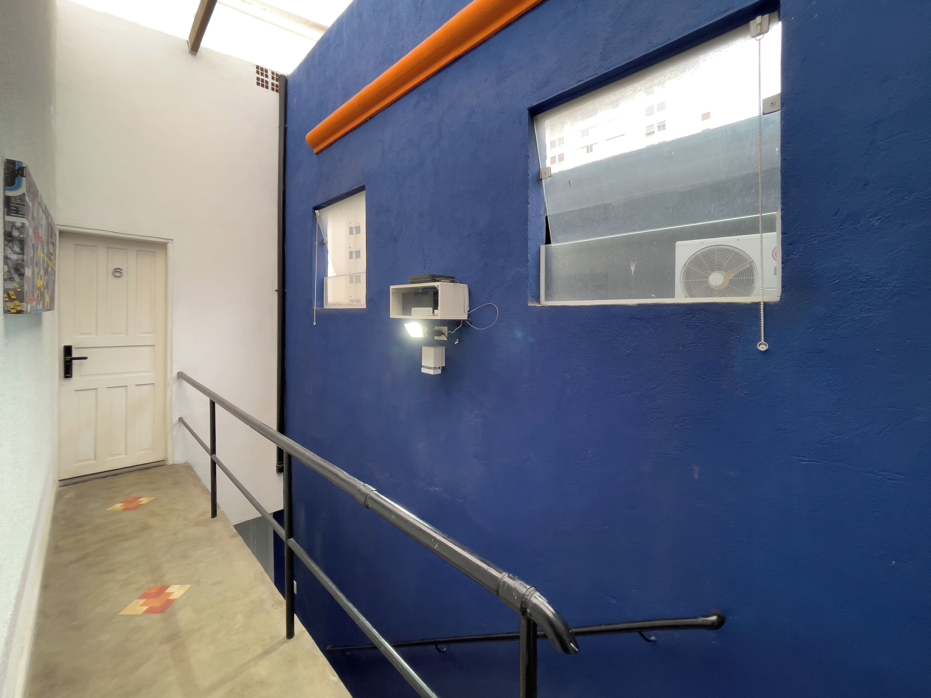 A hallway with a blue wall, a white door, a window with an air conditioning unit, and a handrail.