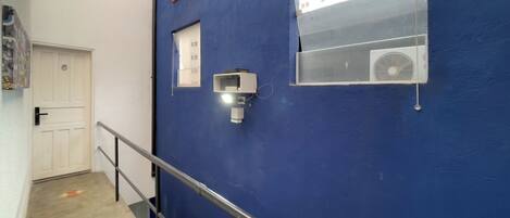 A hallway with a blue wall, a white door, a window with an air conditioning unit, and a handrail.