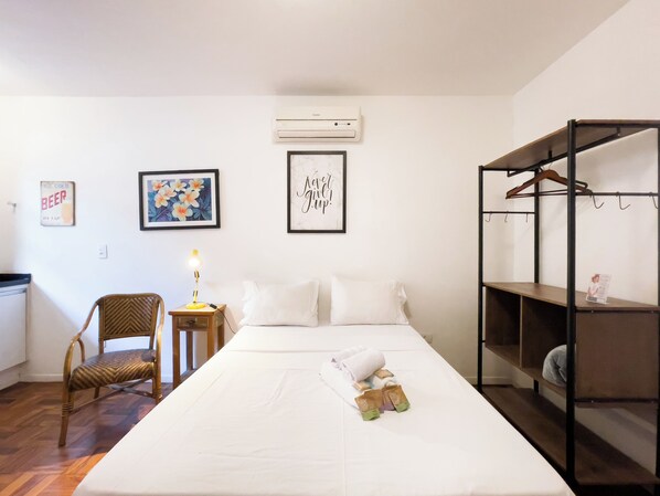 A hotel room with a bed, a chair, a bedside table with a lamp, a wardrobe, and wall decorations. - Coliving Perdizes (São Paulo)
