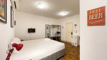 A hotel room with a bed, a red desk lamp, a television, a wardrobe, and a sign that says 'FREE BEER Tomorrow'.