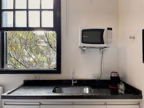 Una cocina con microondas integrado, un lavamanos y una ventana con vista a árboles.