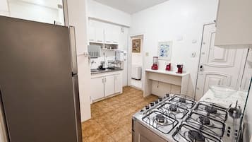 Una cocina compacta con estufa a gas, refrigerador y alacenas blancas.