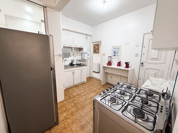 Una cocina compacta con estufa a gas, refrigerador y alacenas blancas.