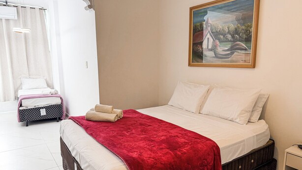 Un dormitorio con cama, un cuadro, una maleta y un radiador.