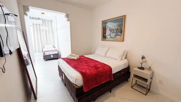 Una habitación de hotel con cama, mesita de noche, un cuadro en la pared y vista al pasillo.
