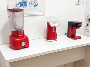 Una encimera de cocina con una licuadora roja, un hervidor eléctrico blanco y una cafetera negra.