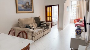 Una sala de estar con un sofá color beige, una mesa de comedor y un cuadro de una escena costera.