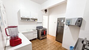 Una cocina con armarios blancos, una licuadora roja, una estufa a gas, un refrigerador de acero inoxidable y un microondas.