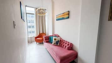 Un pasillo con un sofá rosa, una silla, una lámpara colgante y un cuadro en la pared.